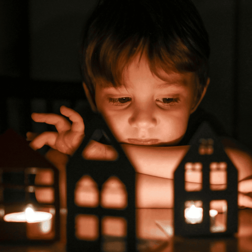 Boşanma Çocukları Nasıl Etkiler 1 - Baltaş Grubu Child sits in dim light, playing with a glowing orange toy city with lit windows and candles nearby.